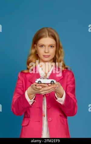 bella donna bionda in giacca rosa che tiene una piccola macchina Foto Stock