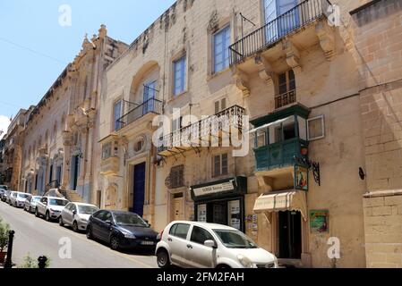 Valletta. Malta. Strada stretta nella Città Vecchia con tipica architettura maltese: Edifici in pietra calcarea con balconi in legno recintati. Foto Stock