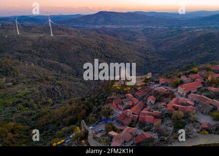 Panorama aereo del drone Sortelha storico villaggio al tramonto con luci sul castello eolico turbine eoliche e paesaggio naturale, in Portogallo Foto Stock