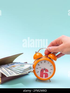 Una mano tiene una sveglia arancione accanto a un portafoglio con dollari USA. Esecuzione rapida del lavoro. Concetto aziendale. Concetto di gestione del tempo aziendale Foto Stock