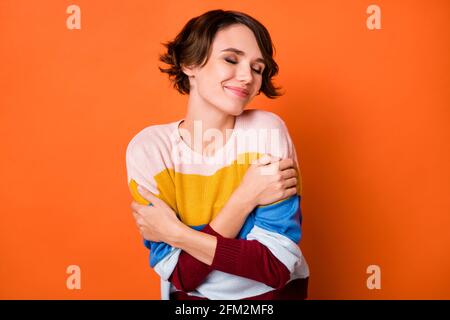 Foto di adorabile giovane signora vestita a strisce abbracciandosi occhi chiusi sfondo di colore arancione isolato Foto Stock