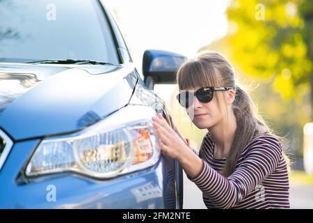 Giovane cliente donna che esamina attentamente una nuova auto presso il negozio all'aperto del concessionario prima di acquistarla. Foto Stock