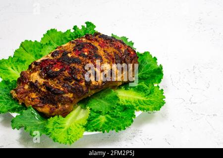 Un grosso pezzo di carne di maiale tritata, cotta in forno, cotta in forno, su foglie di lattuga verde, primo piano. Foto Stock