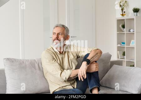Uomo maturo rilassato e premuroso rilassarsi seduto sul divano e pensare a casa. Foto Stock