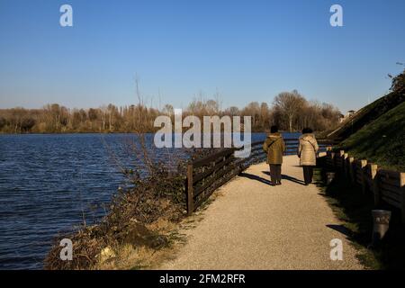 Due donne che camminano su un sentiero vicino alla riva di un lago al tramonto in inverno Foto Stock