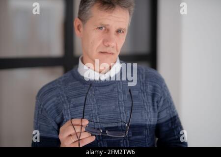 Uomo serio in un maglione e gli occhiali in mano guarda attentamente nel telaio Foto Stock