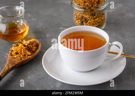 Tè alla calendula in una tazza bianca. Tè alle erbe con fiori di marigold secchi. Foto Stock