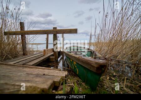Una piccola barca verde che galleggia sul lago vicino al molo Foto Stock