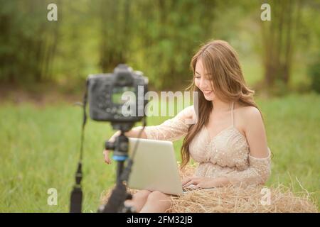 Bella donna seduta in un prato filmare all'aperto, Thailandia Foto Stock