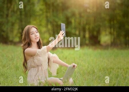 Bella donna seduta in un prato facendo una videochiamata, Thailandia Foto Stock