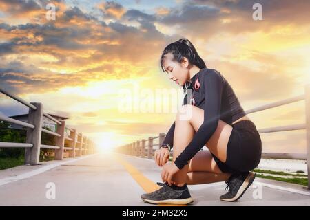 Donna runner accovacciata su un ponte che guarda il suo orologio intelligente all'alba, in Thailandia Foto Stock