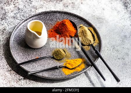 Cucchiai di spezie multicolore su un piatto con un caraffa di olio d'oliva Foto Stock