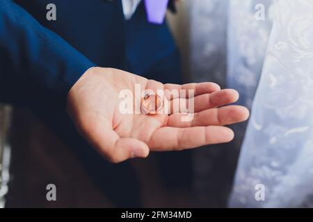 Sul palmo di un uomo ci sono due anelli di nozze. Lo sposo tiene gli anelli. Tradizione nuziale. Gli anelli d'oro giacciono sul palmo di un uomo Foto Stock