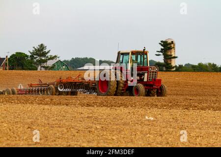 Chestertown, MD, USA 05-02-2021: Un trattore internazionale 1586 a sei ruote rosso con cabina sta arando un campo agricolo vuoto in primavera. Ci sono Foto Stock