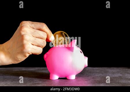 Immagine concettuale per l'utilizzo della valuta crittografica digitale per il risparmio. Una donna caucasica sta mettendo una moneta simbolica di Ethereum (ETH) in una banca di piggy come un risparmio Foto Stock