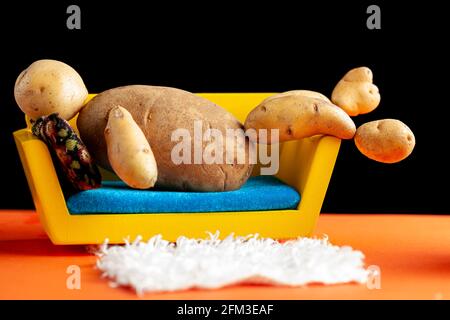 Un'immagine concettuale metaforica bizzarra che mostra un uomo di patate sdraiato su un divano in un ambiente di soggiorno. Immagine del lettino patata, obesità, sedentario l Foto Stock