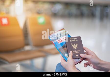 Libro con passaporto e guida di viaggio per le donne in mano in Thailandia all'aeroporto, a causa del concetto di pandemia epidemica di Covid-19. Foto Stock