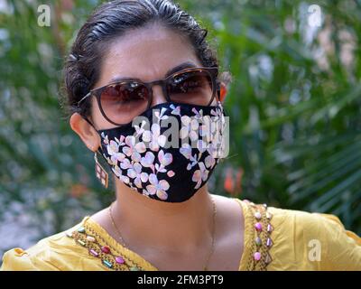 Bella giovane donna messicana affascinante con occhiali da sole marroni indossa una maschera elegante e posa per la fotocamera durante la pandemia di virus corona. Foto Stock
