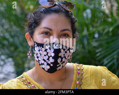 La giovane donna messicana responsabile con gli occhi marroni indossa una maschera elegante in tessuto e posa per la fotocamera durante la pandemia del virus corona. Foto Stock