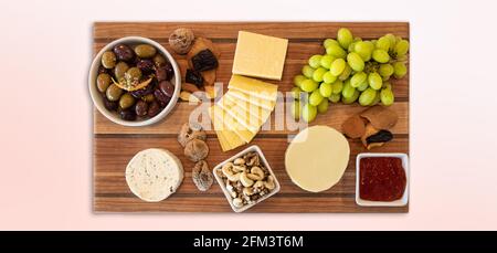 Assortimento di formaggi su tavola di legno con frutta, noci, gelatina e olive. Foto Stock