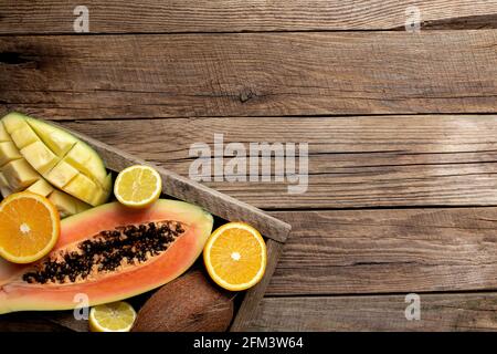 Frutta tropicale fresca in una scatola di consegna di legno su sfondo di legno. Papaya, arancio, cocco, mango e limone vista dall'alto piatto con spazio per la copia Foto Stock