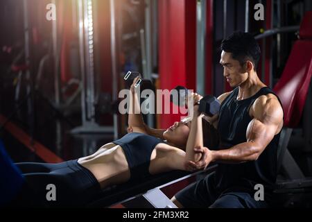 Personal fitness trainer che aiuta la donna a praticare manubri. Personal trainer in palestra fitness Foto Stock