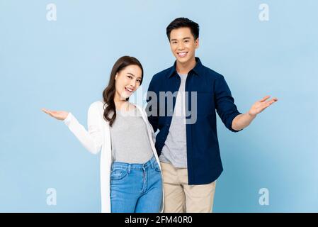 Annuncio ritratto di felice allegra coppia asiatica impressionante con grande sorrisi aprendo le mani su uno sfondo azzurro isolato Foto Stock