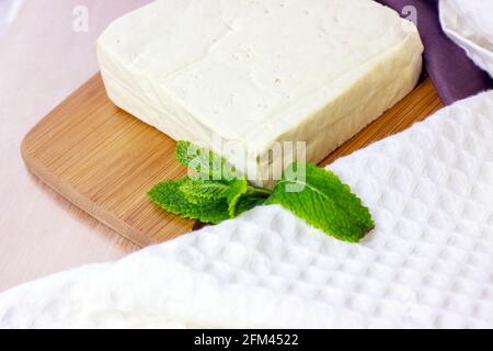 Fette di tofu vegetariano crudo con menta fresca su sfondo di legno. Foto Stock