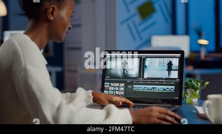 Videografo africano che lavora su un computer portatile dall'ufficio aziendale, editing di filmati e audio di notte. Creazione di contenuti utilizzando dispositivi professionali moderna tecnologia di elaborazione wireless montaggio film. Foto Stock