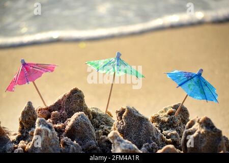 Tre piccoli ombrelloni in carta per cocktail stand nella sabbia Foto Stock