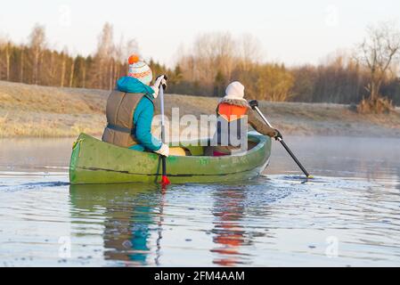 madre e figlia che girovagano una canoa in primavera nella mattina presto. stile di vita attivo. Mattina paesaggio, nebbia dal fiume mattina e la gente su Foto Stock