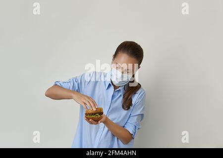 Bella giovane donna che cucinava hamburger vegano in maschera protettiva Foto Stock