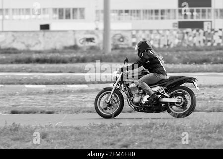 Ulyanovsk, Russia - 10 giugno 2017. La ragazza in una giacca nera e pantaloni grigi gareggia su una moto. Sfocatura del movimento. Immagine in bianco e nero. Foto Stock