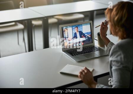 Donna che punta con la penna allo schermo del laptop durante la riunione online Foto Stock