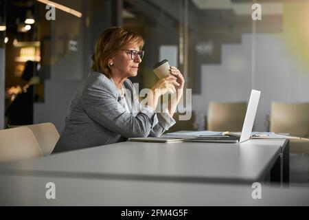 Donna d'affari che beve caffè di fronte al computer portatile Foto Stock