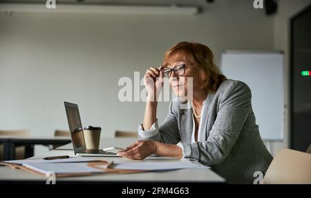 Femmina che regola i suoi occhiali mentre legge i record di carta Foto Stock
