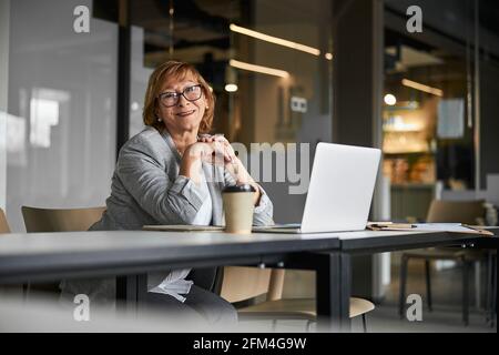Accogliente donna d'affari sorridente alla macchina fotografica, seduto vicino al computer portatile Foto Stock