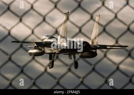 United States Air Force McDonnell Douglas F-15 volo da caccia Eagle Jet atterrando a RAF Lakenheath, Suffolk, Regno Unito, dietro la recinzione di sicurezza perimetrale Foto Stock