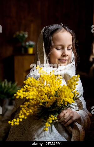 una bambina in un fazzoletto con una mimosa Foto Stock