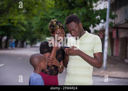Felice famiglia moderna, padre, madre e figlio che visitano la città insieme. Genitori che controllano i contenuti dello smartphone. Foto Stock