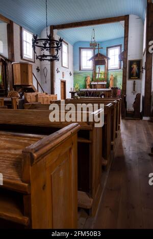 Interno di una vecchia chiesa in legno. Soffitti blu, pareti bianche, banchi di legno, sculture folcloristiche sull'altare. Crepuscolo naturale per una luce soffusa. Foto Stock