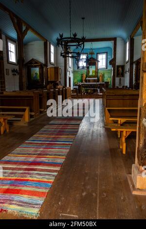 Interno di una vecchia chiesa in legno. Soffitti blu, pareti bianche, banchi di legno, sculture folcloristiche sull'altare. Crepuscolo naturale per una luce soffusa. Foto Stock