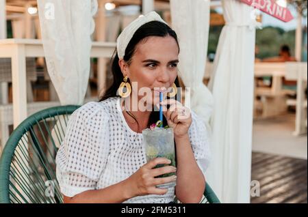 Ritratto di giovane donna felice e sorridente che beve un cocktail mojito nel bar estivo. Foto Stock