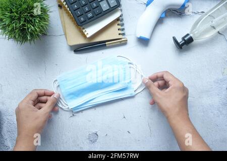 mano dell'uomo che tiene la maschera chirurgica del viso sul tavolo Foto Stock