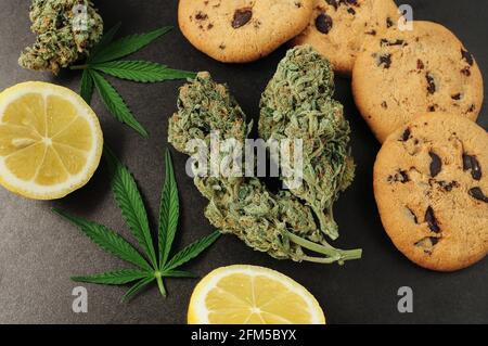 Dolci con olio CBD. Gemme di marijuana su sfondo nero. Fiori di cannabis e biscotti al cioccolato con noci primo piano. Vista dall'alto, disposizione piatta. Foto Stock
