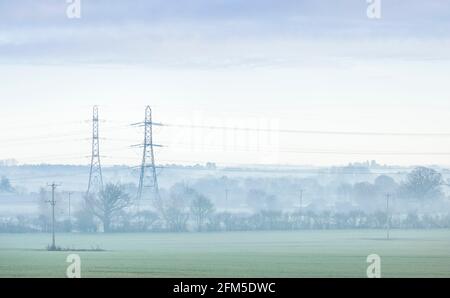 Tralicci elettrici in un paesaggio britannico in una mattina misteriosa. Aylesbury vale, Buckinghamshire, Regno Unito Foto Stock