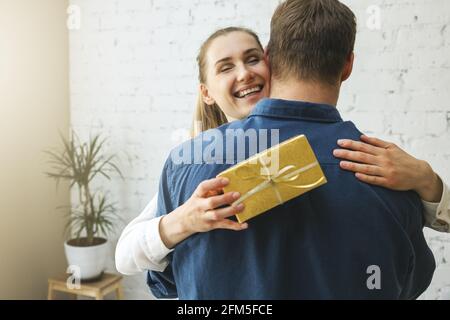 donna di ringraziamento con scatola regalo che abbracciano il marito a casa. compleanno o anniversario sorpresa Foto Stock