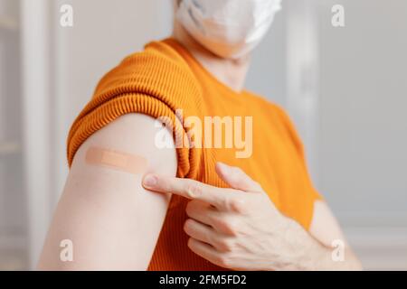 Uomo in maschera mostrando la sua spalla con bendaggio dopo aver ottenuto una vaccinazione Foto Stock