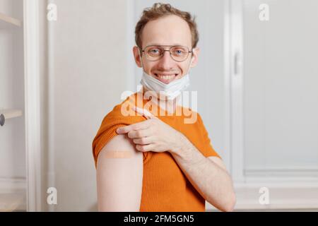 Giovane caucasico sorridente che mostra la sua spalla con bendaggio dopo ottenere una vaccinazione Foto Stock