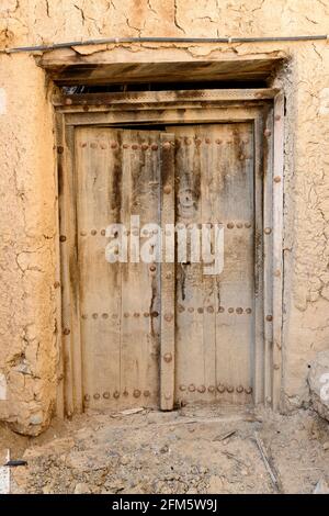 Al Hamra. Regione ad Dakhiliyah, Oman. Porta in legno nella parte vecchia della città con case abbandonate in rovina . Foto Stock